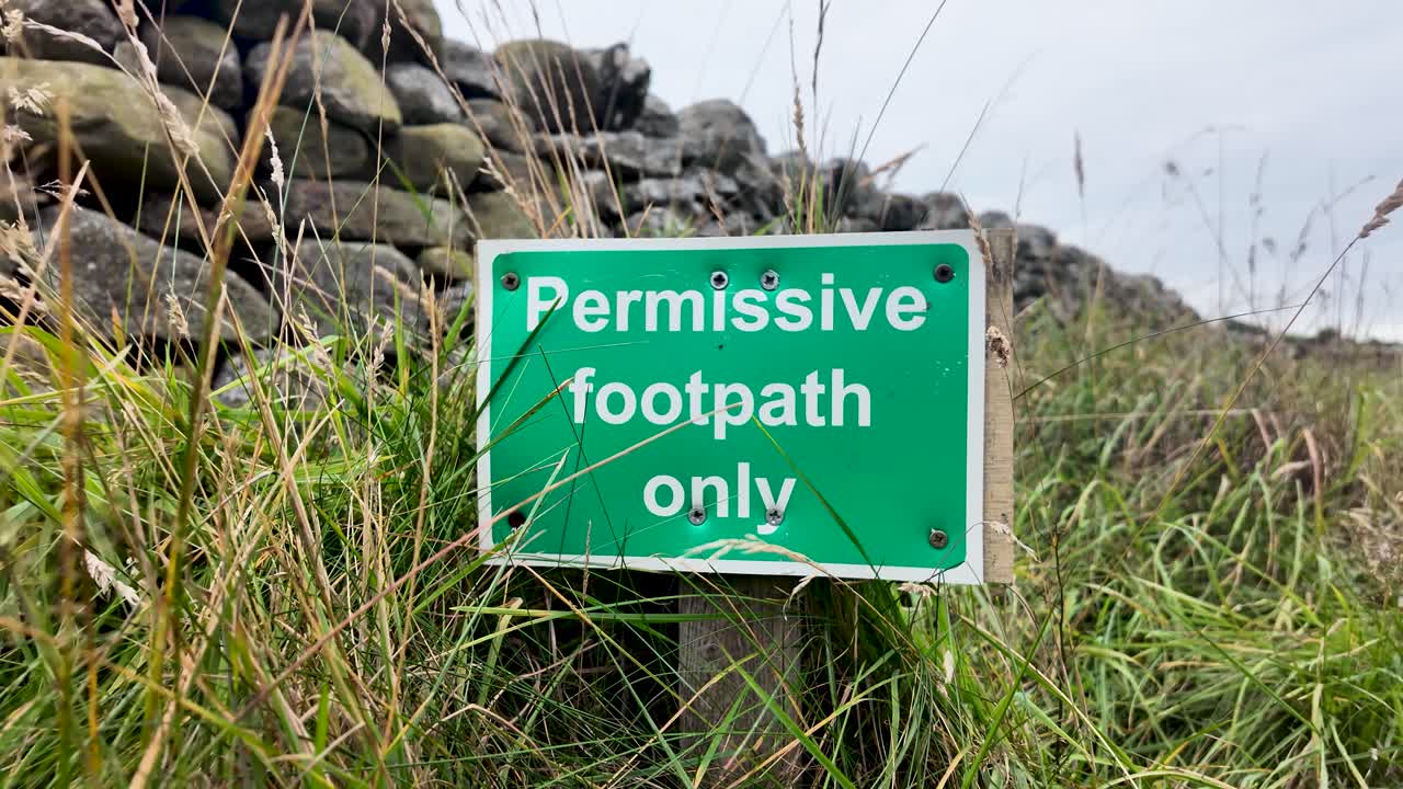Green permissive footpath only sign in the grass, with dry stone wall in the background, County Durham, England