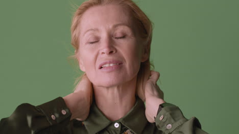 vista de cerca de una mujer rubia madura con camisa verde posando en la cámara tocando su cabello mientras el viento mueve su cabello y camisa sobre fondo verde 1