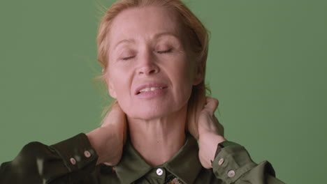 close-up beeld van blonde rijpe vrouw die een groen shirt draagt dat zich voor de camera bevindt terwijl ze haar haar aanraakt terwijl de wind haar haar en shirt op groene achtergrond beweegt 1