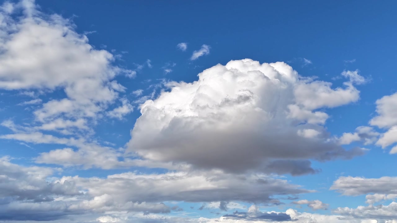 4K drone timelapse focuses on the evolution of a white cloud shifting shape as it moves across a bright blue sky. Cinematic atmospheric motion captures the natural development of a cloudscape.
