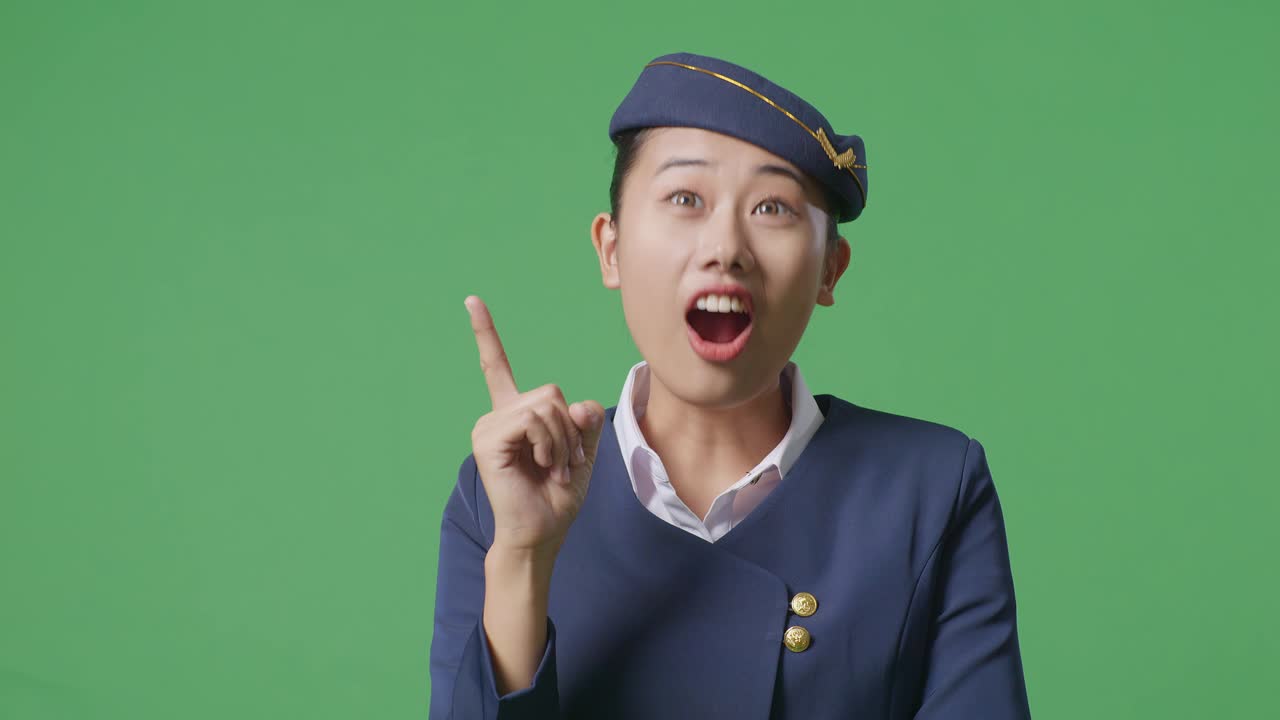 아시아 여성 승무원이 생각하고 주위를 둘러보며 초록색 스크린 배경 스튜디오에 서있는 동안 지표손가락을 들어 올립니다.