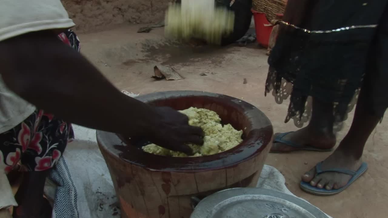 Pasta di manioca in un mortaio di legno durante il tradizionale processo di pestatura nel Ghana rurale, piedi di donne visibili attorno al contenitore