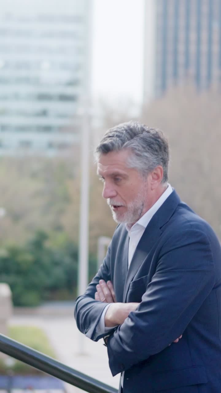 A businessman in a suit standing outdoors in an urban setting, engaging in conversation or deep thought
