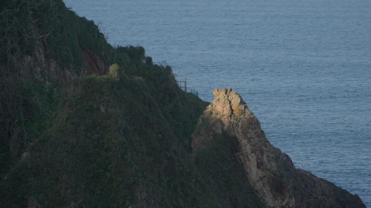 Dramatic rocky cliff covered with green vegetation overlooking the Atlantic Ocean near Candás in Asturias, Spain. Scenic coastal landscape with rugged cliffs and calm blue sea along northern Spain.