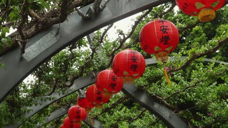 chinese lanterns sway in the wind underneath a grassy archway.