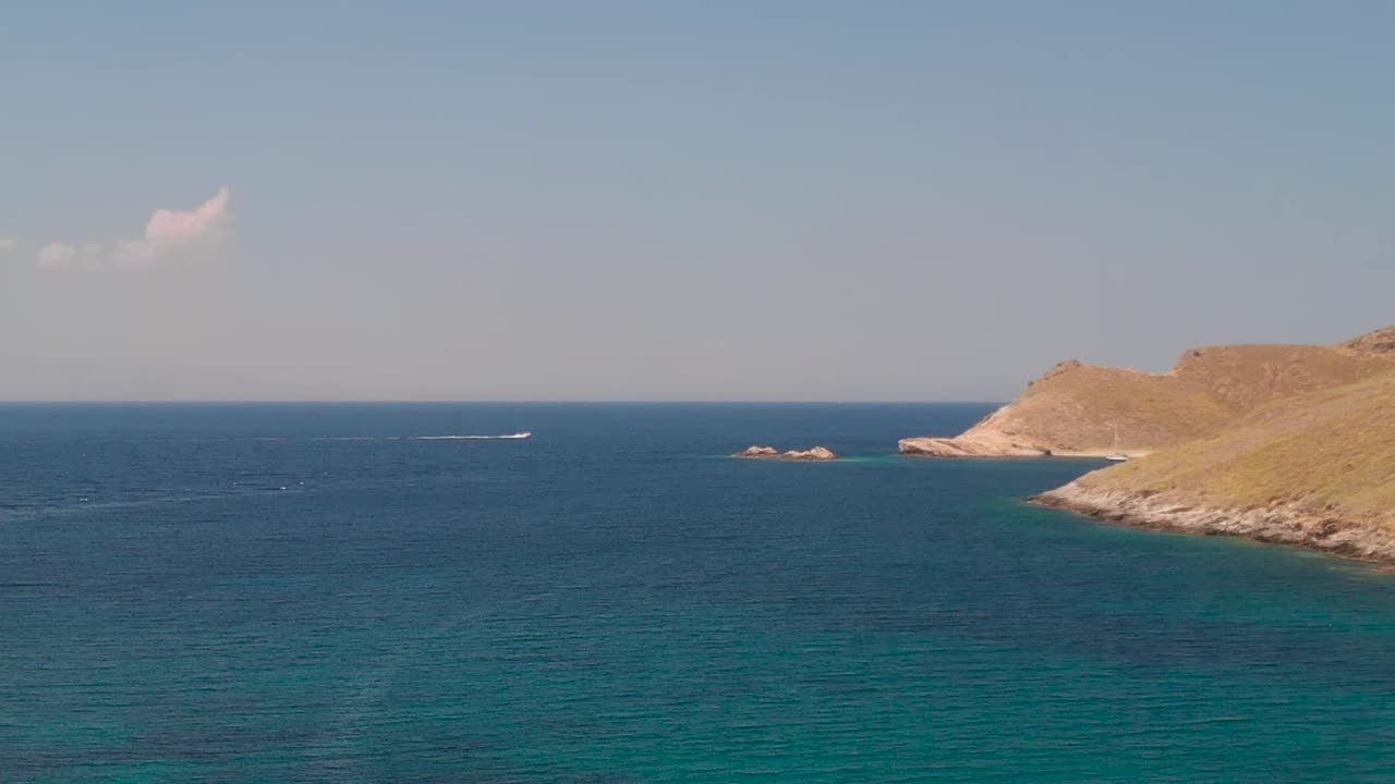 alto avance aéreo sobre el océano hasta las colinas y lancha rápida en la distancia