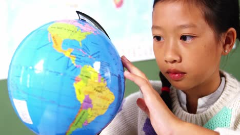 schoolgirl looking at globe in classroom at school