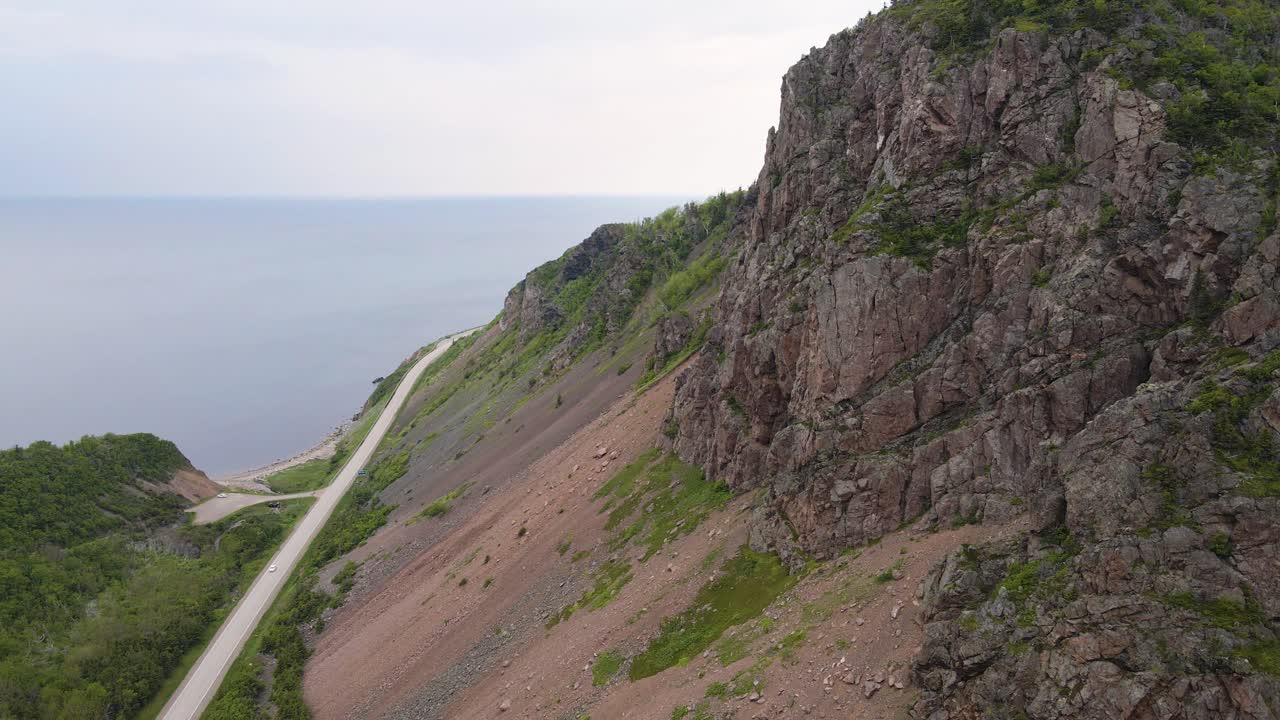 Drone shot panning downwards of a massive mountain off the cost of the Atlantic Ocean on the famous Cabot Trail, Cape Breton Island in Nova Scotia shot during the summer in 4k