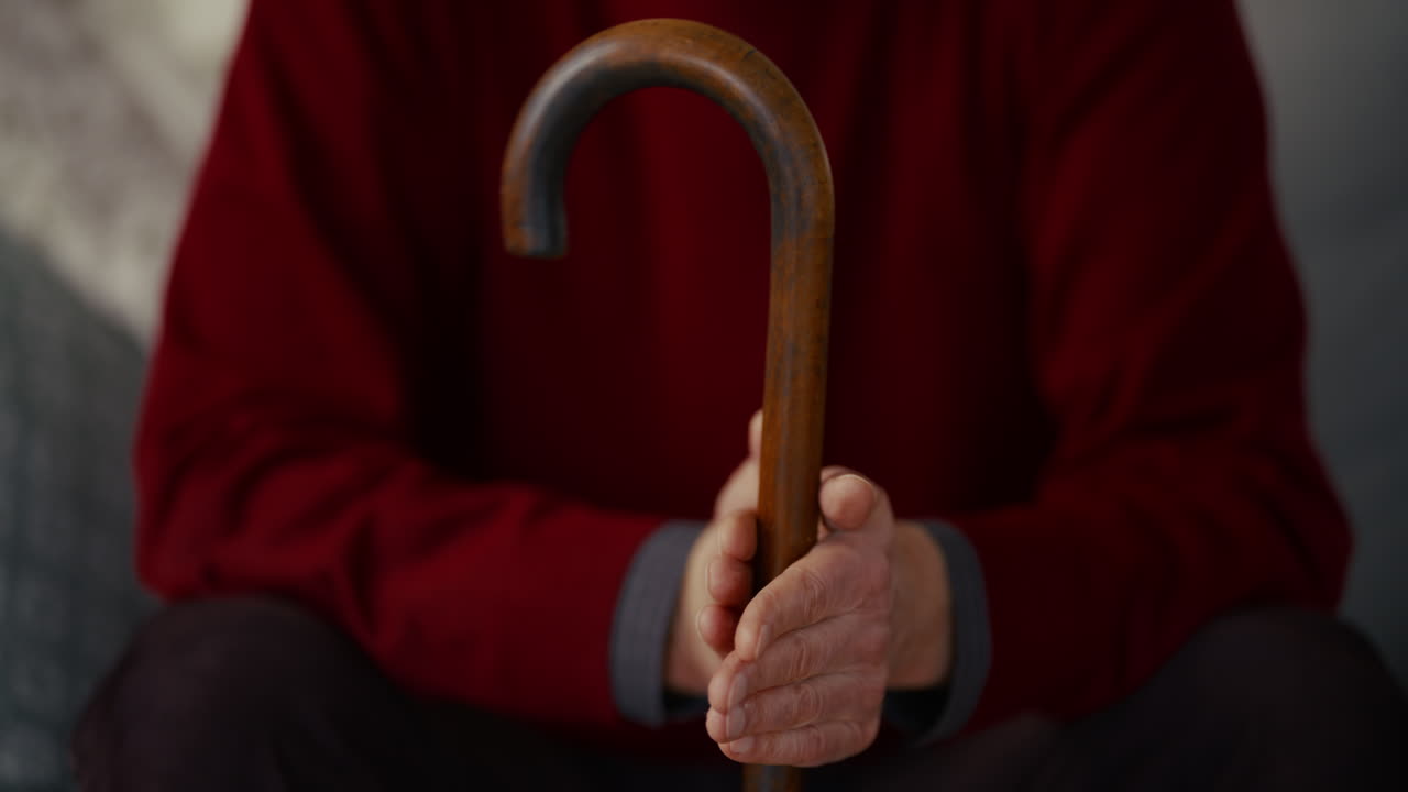 Primo piano delle mani di un anziano che tengono un bastone da passeggio di legno
