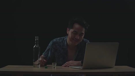 hombre asiático borracho bebiendo vodka durante una llamada de video en una computadora portátil con fondo negro