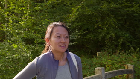 woman wearing sports clothing carrying yoga mat standing on bridge in forest looking around enjoying peace and beauty of nature 2