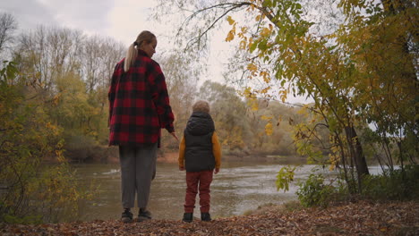 Una-Mujer-Con-Un-Niño-Pequeño-Descansa-En-La-Naturaleza-Parada-En-La-Orilla-De-Un-Lago-Tranquilo-Y-Contempla-El-Paisaje-En-Las-Vacaciones-Familiares-Del-Día-De-Otoño-En-El-Bosque