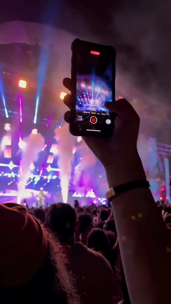 Una vivace scena di un concerto catturata da una angolazione bassa, concentrandosi su un video registrato da un telefono