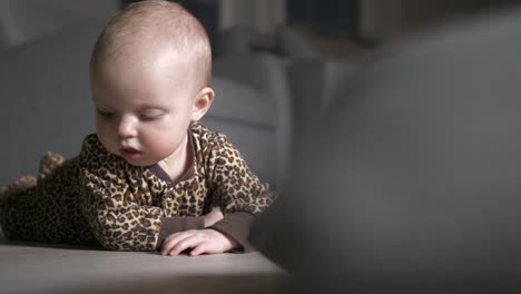 Baby-in-cute-onesie-clothing-rolls-on-floor-in-home-setting