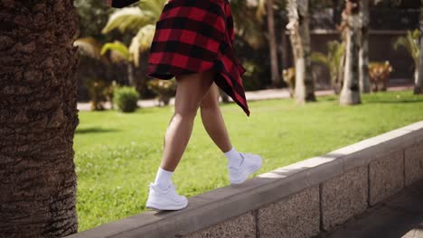 chica de moda está en el parapeto, el equilibrio. chica turística de moda caminando a lo largo de los árboles tropicales parque en el parapeto. mujer elegante elegante disfrutar del tiempo. vista rara