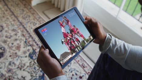 Composite-of-man-sitting-at-home,-watching-sports-event-on-tablet