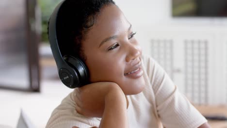 Feliz-Mujer-Afroamericana-Sentada-En-El-Sofá-Usando-Auriculares-Y-Escuchando-Música,-Cámara-Lenta