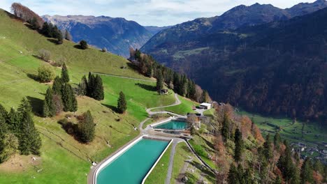aerial flyover shot of water reservoir for hydropower plant in swiss mountains. village in valley. sunny day in fall season. wide shot.