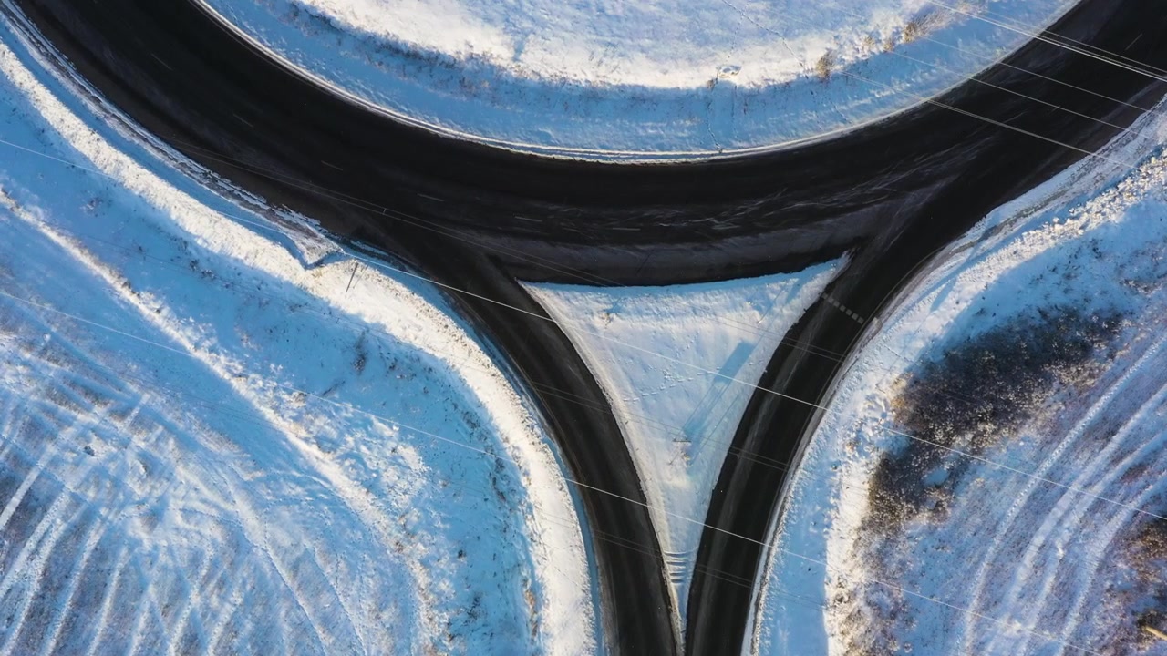 Surreal drone flight creating a mirror effect over a snowy road splitting into a Y-junction