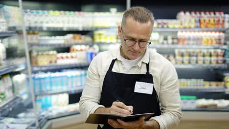 retrato de un asistente de ventas con gafas con un cuaderno y un lápiz en las manos en una tienda de comestibles.