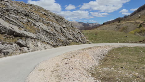a winding, narrow mountain road snakes its way through the landscape with snow on top of the mountain under a blue sky with clouds. sunny day, wide shot, slow motion
