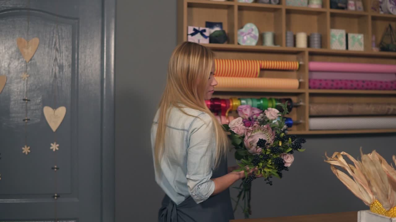 Young attractive florist starting to arrange modern bouquet in the flower shot, young handsome florists work at flowers shot