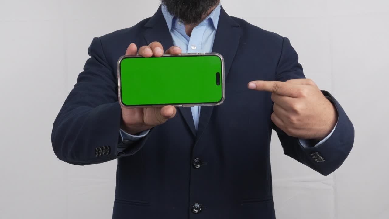 Uomo in abito che indica uno smartphone in modalità orizzontale con schermo verde, mockup mobile, video 4K.