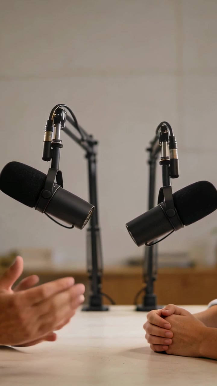 L'ospite di sinistra entra, gesticolando mentre l'ospite di destra tiene le mani giunte, i microfoni registrano un podcast.