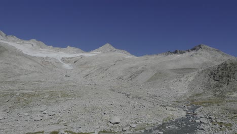 Drone-captures-a-man-approaching-a-small-bridge-on-a-glacier-river-trail