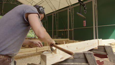 carpenter using axe to remove pieces of wood from massive log