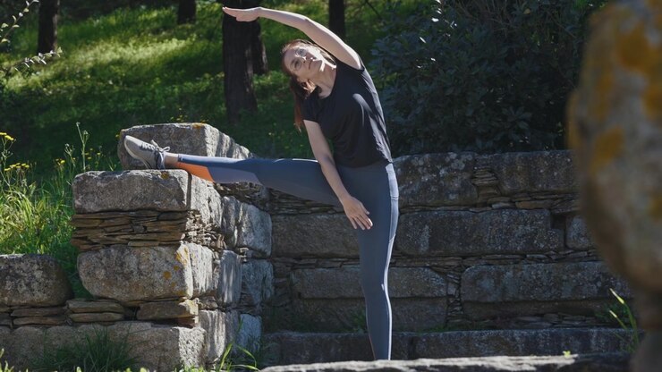 Sports woman does stretching in nature throwing a foot on a stone wall