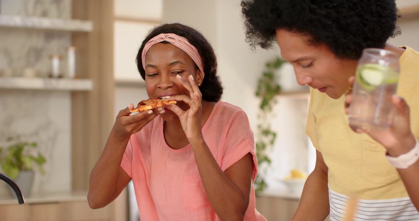 Après le geste de la femme, un couple afro-américain riant, mangeant de la pizza dans la cuisine, tenant une carafe d'eau.