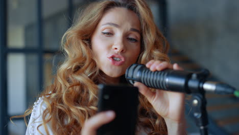 Vocalist-singing-in-microphone.-Focused-woman-learning-song-text-on-smartphone