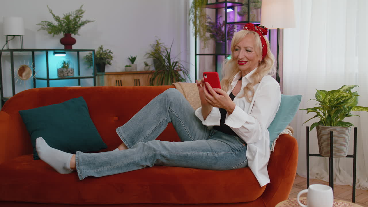 abuela mayor sentada en el sofá, usando el teléfono inteligente para compartir mensajes en la aplicación de redes sociales