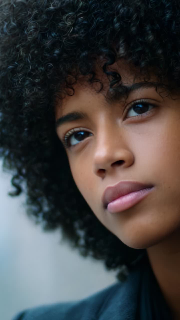 Close-Up Portrait of a Thoughtful Young Woman with Curly Hair, Showcasing Her Expressive Eyes and Natural Beauty in a Soft Focus Setting