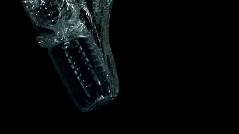 botella de plástico cayendo en el agua sobre un fondo negro