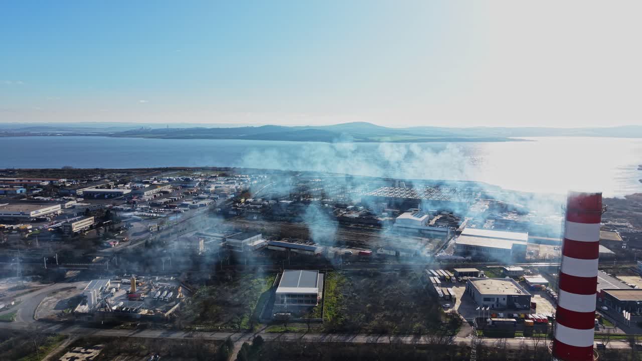 Smoke rises over industrial area near the coast during clear day