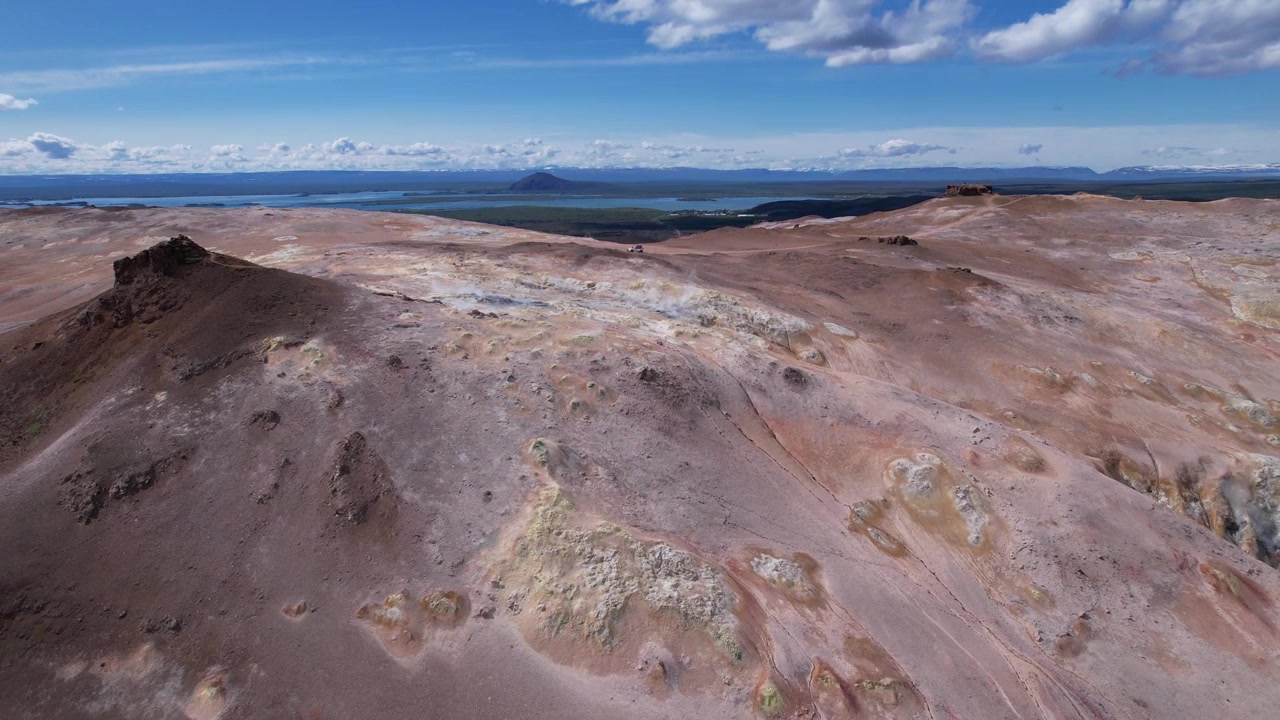 Vista aérea de drone das encostas geotérmicas em Namafjall Hverir, perto do Lago Myvatn, na Islândia, apresentando cristas vulcânicas, depósitos minerais, terreno geotérmico e lago distante