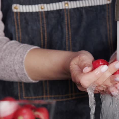 a woman washes radishes under a stream of water from a kitchen tap