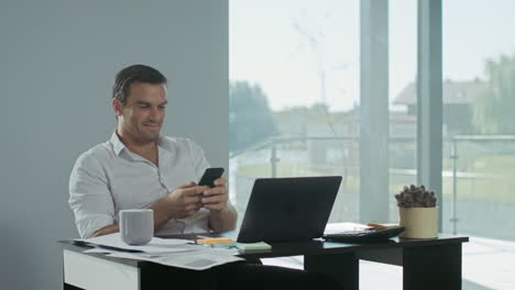 Business-man-scrolling-mobile-phone-at-work-place.-Smiling-man-having-break.