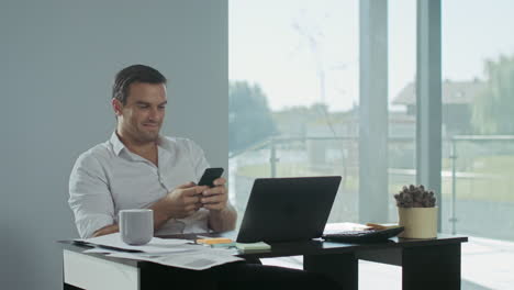 business man scrolling mobile phone at work place. smiling man having break.