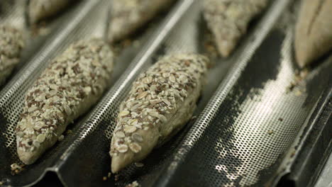 baker taking dough on baguette tray after proofing and dipping it on multi grains inside the bakery