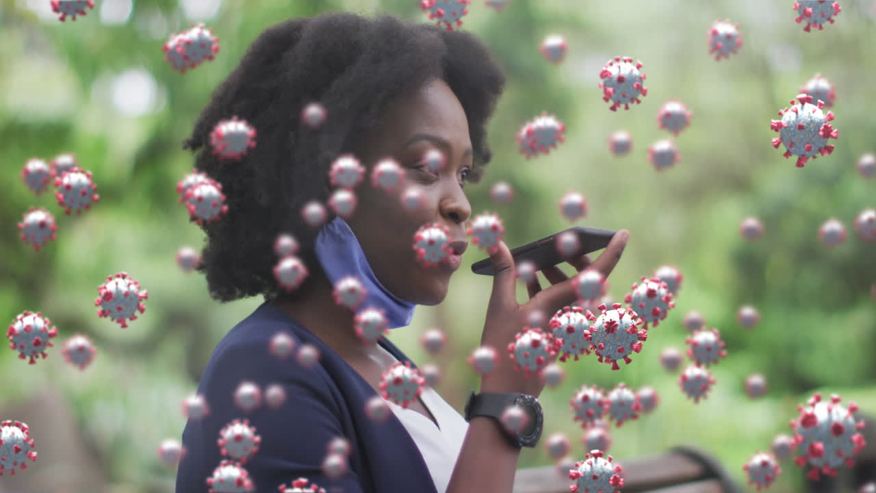 animación de células de coronavirus sobre mujer afroamericana con máscara facial hablando por teléfono en el parque