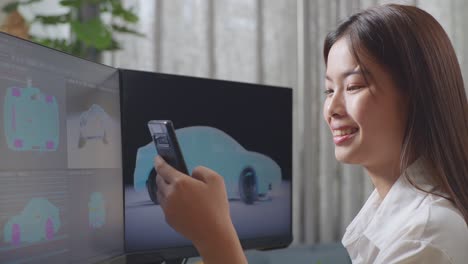 close up side view of asian female automotive designer comparing the 3d model of ev car on the desktop computers to the photo on her smartphone in the studio