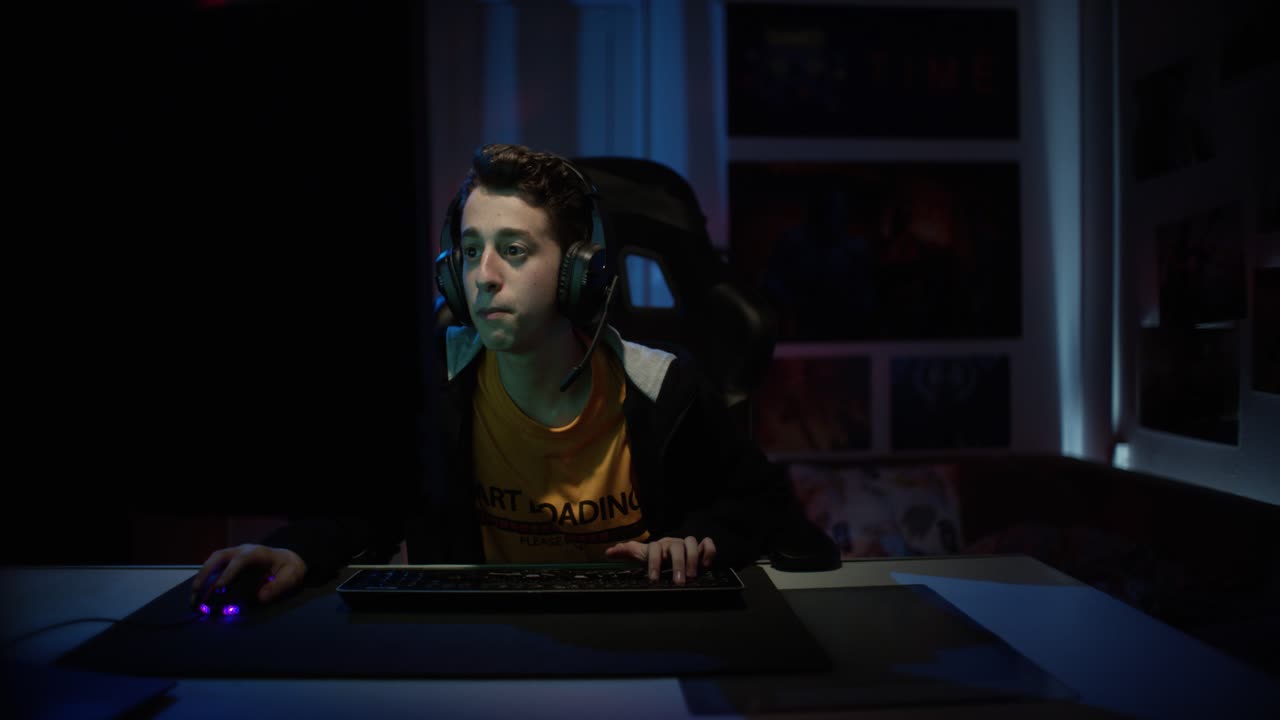 Excited and super concentrated Gamer Playing in Online Video Game on His Personal Computer with big headphones and talking to his teammates via microphone