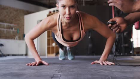video de un entrenador afroamericano motivando a una mujer caucásica para hacer flexiones