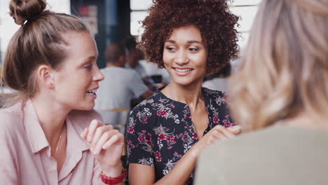 three young female friends meeting sitting at table in coffee shop talking