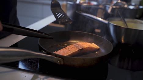 close up shot of chef cooking fresh salmon fish steak in hot pan in kitchen of restaurant