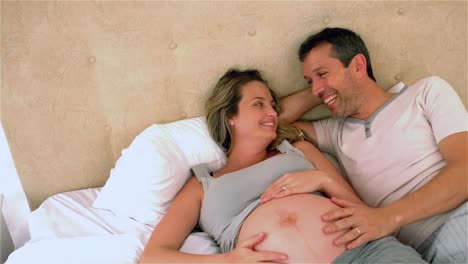 Happy-future-parents-talking-on-bed-and-touching-belly