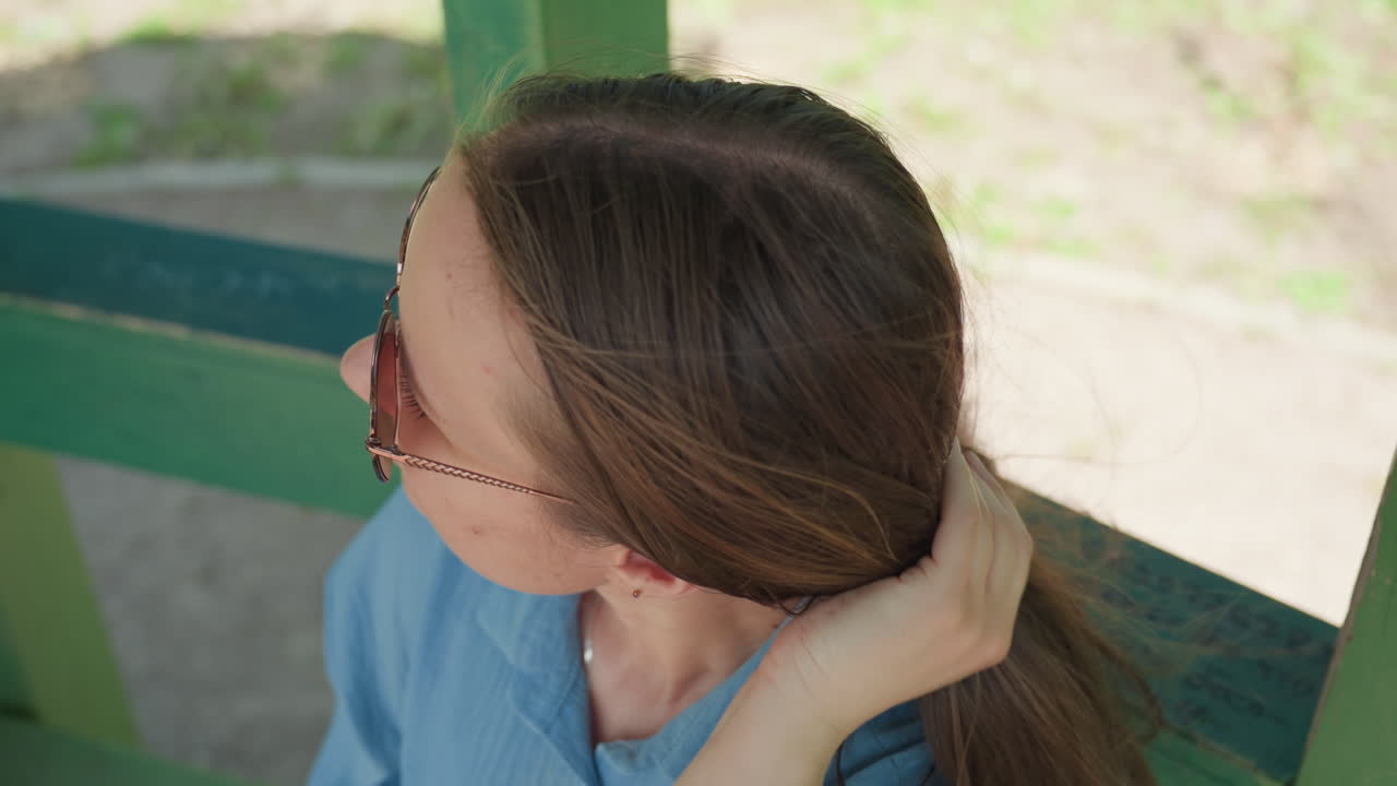 선글라스를 낀 자신감 넘치는 여성, 공원 벤치에 앉아 세련된 옷을 입은 여성, 도시를 배경으로 녹지대에 앉아 선글라스를 고쳐 쓰는 패셔너블한 여성 모델 (에디토리얼 이미지)